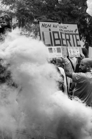 Un nuage de fumée cache partiellement un homme qui porte une pancarte disant "Liberté" lors d'une manifestation Brestoise
